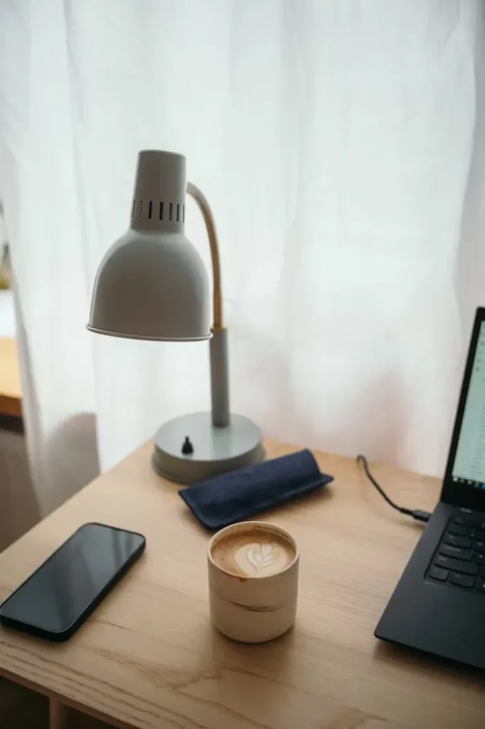 Smartphone auf hellem Holzschreibtisch neben Kaffeetasse und Laptop – Symbol für digitalen Minimalismus und weniger Ablenkung durch Benachrichtigungen